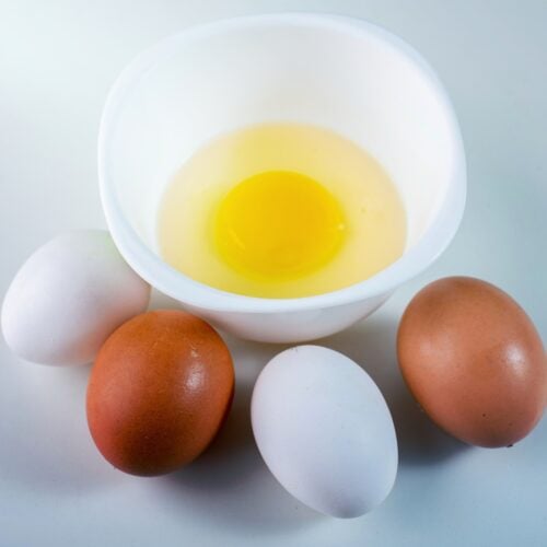 A small white bowl with raw egg in it is on the light surface. The four eggs lie in front of it | Hurry The Food Up