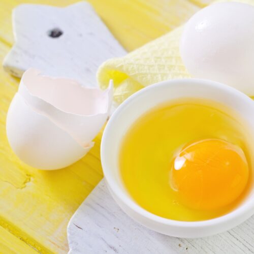 A small white bowl with raw egg is on the wooden cut board. There are some eggshells near it | Hurry The Food Up
