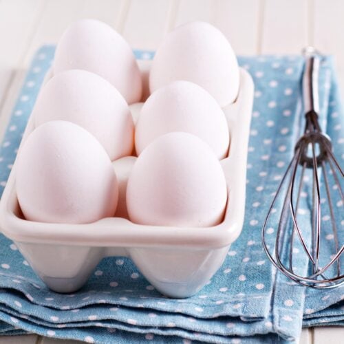 A carton of eggs is on the light blue kitchen towel. Near it, there is an egg beater | Hurry The Food Up