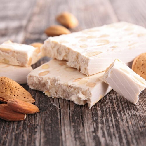 A few nuts and pieces of nougat are on a wooden surface