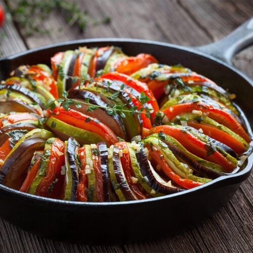 Vegetable ratatouille baked in cast iron frying pan. It stands on a wooden surface