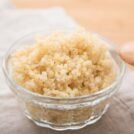 A transparent bowl of cooked quinoa with wooden spoon