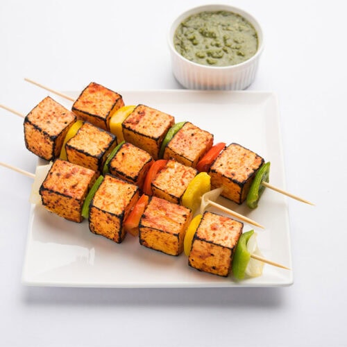 Paneer tikka on a plate with a ramekin of green sauce