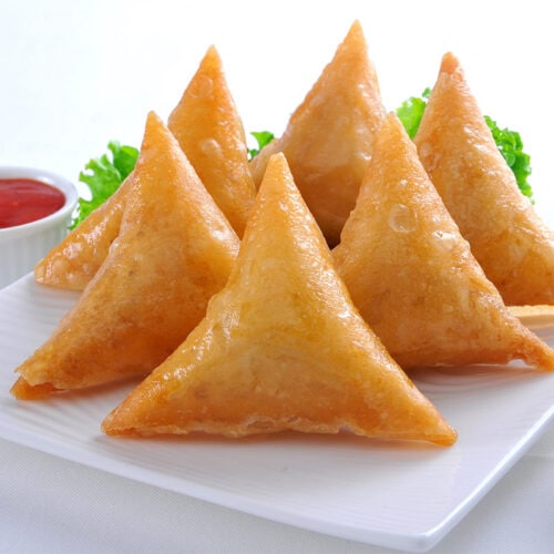 Samosas on a plate. Two ramekins with chutney next to the plate