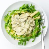 A bowl of creamy vegan mushroom pasta topped with fresh arugula.