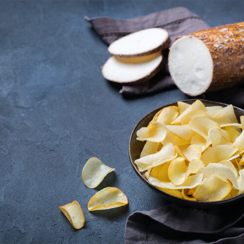 Yuca root with a plate of chips on black surface