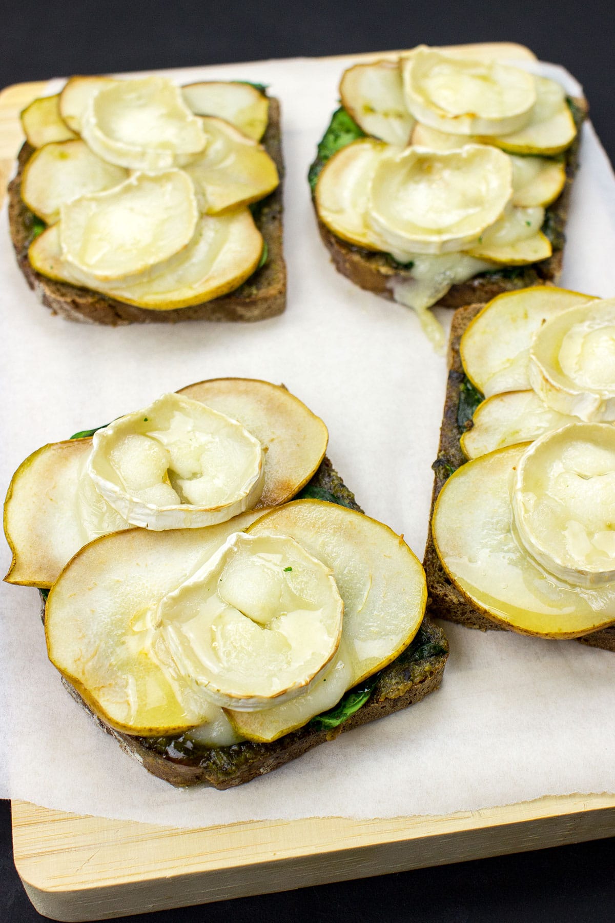 Slices of Honey Pesto Goat Cheese Toast, topped with creamy goat cheese, drizzled with golden honey, and garnished with fresh herbs, sit elegantly on a cutting board.