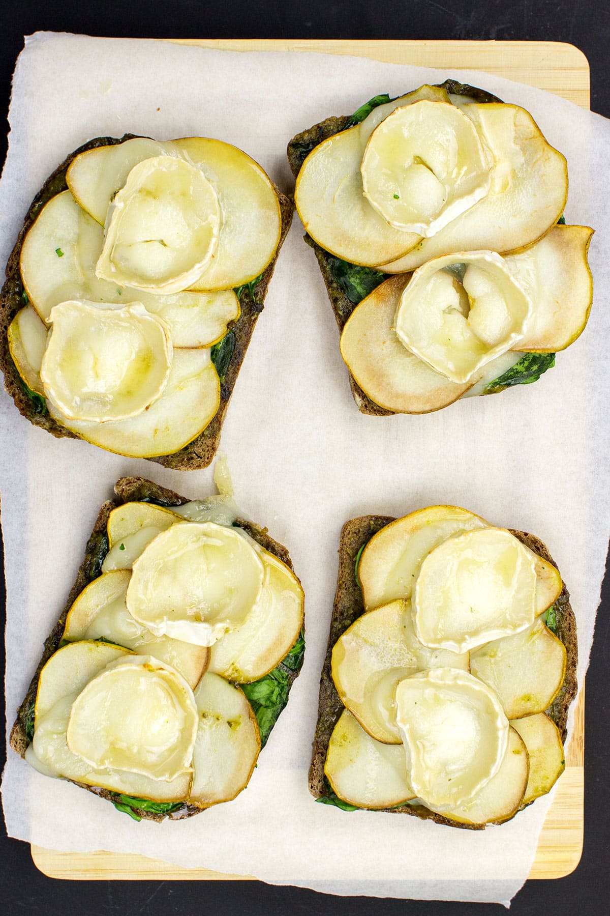 Slices of Honey Pesto Goat Cheese Toast, topped with creamy goat cheese, drizzled with golden honey, and garnished with fresh herbs, sit elegantly on a cutting board.