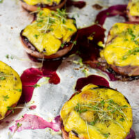 Grilled cherry tomatoes topped with melted yellow cheese and microgreens, served on a foil-lined baking tray with drizzles of savory blueberry jam. - 5