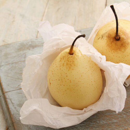 Two yali pears are wrapped in white paper that are on a cutting board