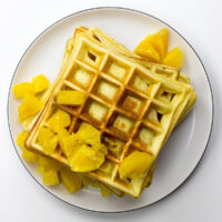 A stack of Orange Buttermilk Waffles, golden and fluffy, topped with fresh orange slices and a dusting of powdered sugar, sits beautifully on a plate. - 4