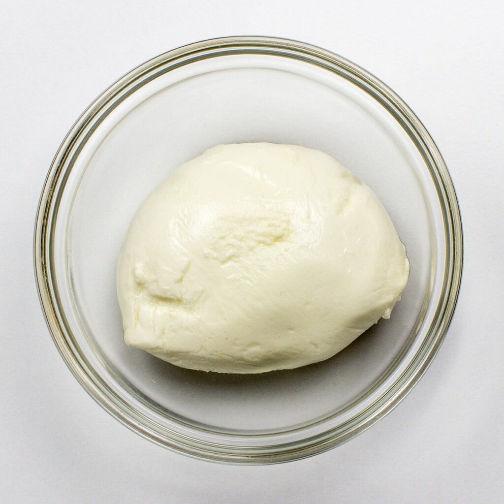 Mozzarella ball in a transparent bowl on white surface