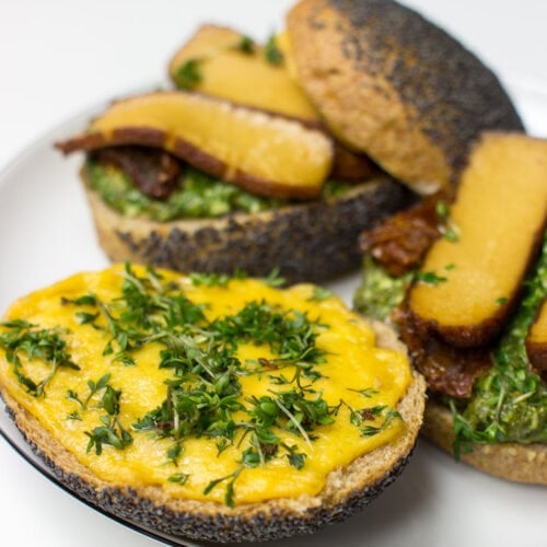 A Tofu Pesto Sandwich with crispy bread, layered with marinated tofu, fresh greens, and a generous spread of vibrant pesto, sits on a plate, ready to be enjoyed.